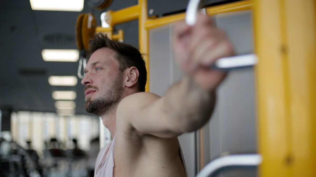 Muscular man exercising on gym equipment, demonstrating strength and focus in a fitness environment.